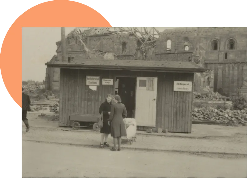 Zwei Frauen im Gespräch vor Laden, im Hintergrund zerstörte Propsteikirche.