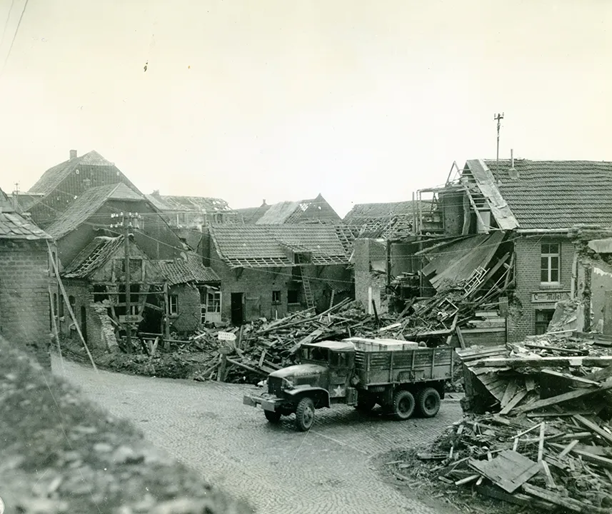 Militärfahrzeug an Kreuzung, dahinter komplett zerstörte Häuser.